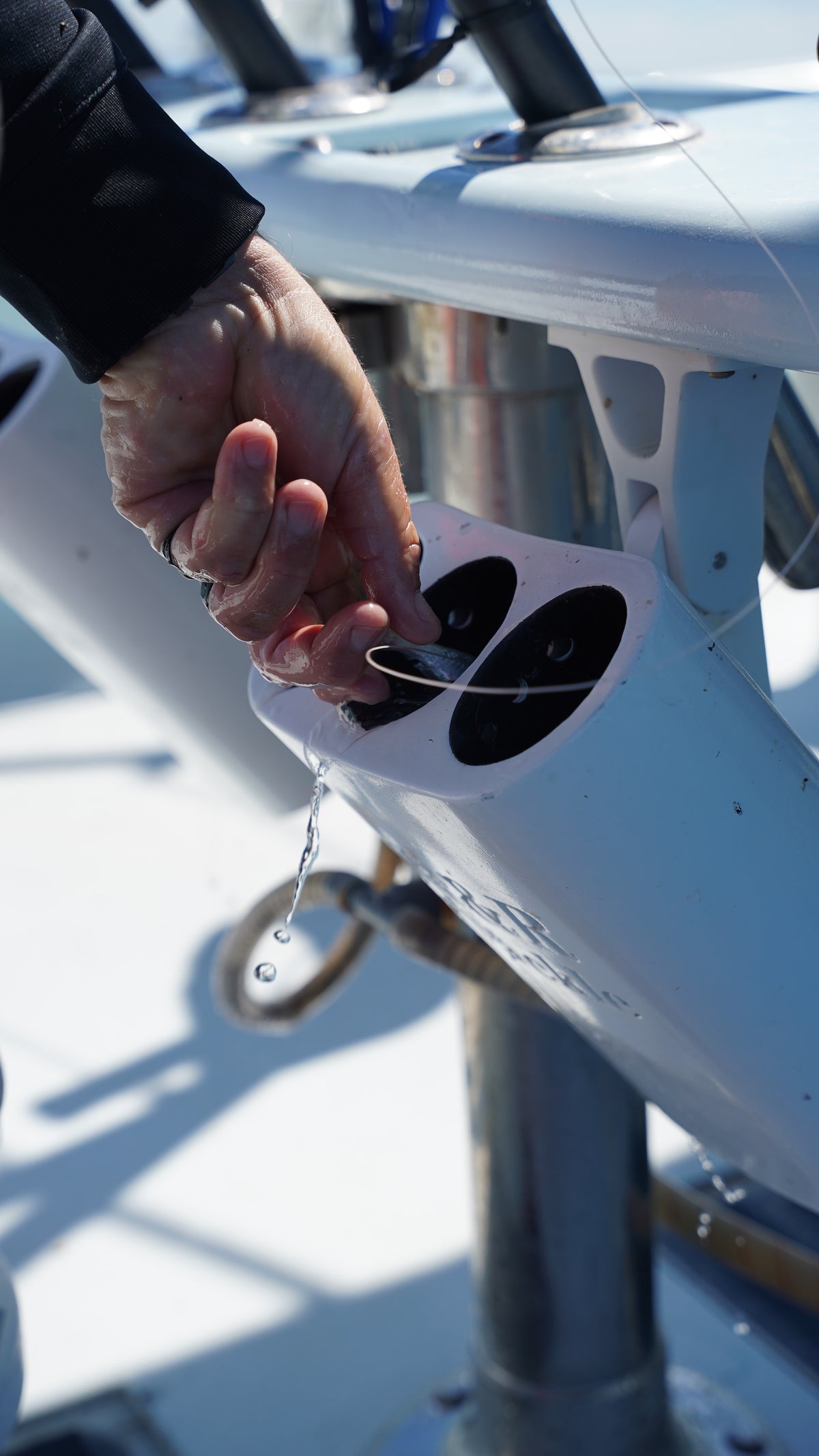 Angler placing a baitfish into an R&R Tackle bait tube mounted aboard a fishing boat, with water draining from the opening.