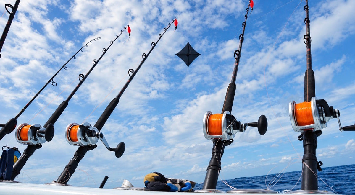 Kite fishing setup aboard an offshore boat, with orange-spooled reels, red floats, and a black kite flying overhead.